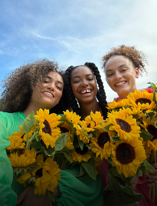 Tarkka ja värikäs selfie kolmesta ihmisestä, jotka pitelevät kukkia käsissään.